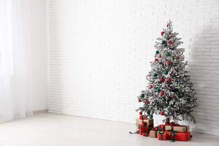 Christmas tree and gift boxes near white brick wall in roomの写真素材