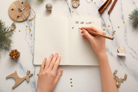 Woman writing to-do list with Christmas decor on white grunge background