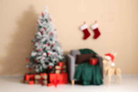 Beautiful Christmas tree and armchair with decorations near beige wall in room. Blurred viewの写真素材
