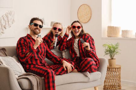 Happy family in sunglasses with remote controls and microphone singing karaoke on sofa at homeの写真素材