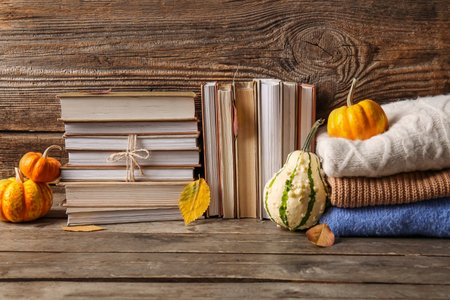 Composition with different books, warm clothes and pumpkins on wooden tableの写真素材