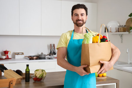Handsome bearded man with bag of food in kitchenの写真素材