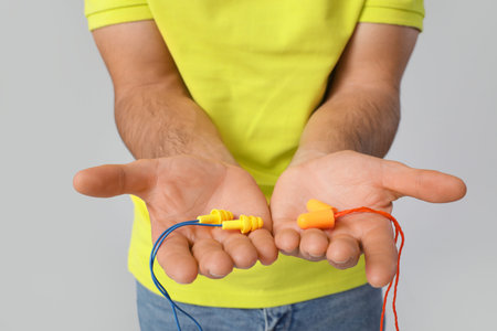 Young man with earplugs on gray background, closeup