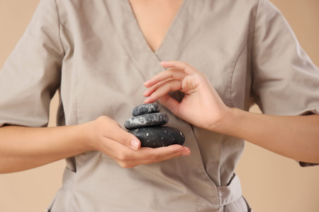 Female massage therapist with spa stones on beige background