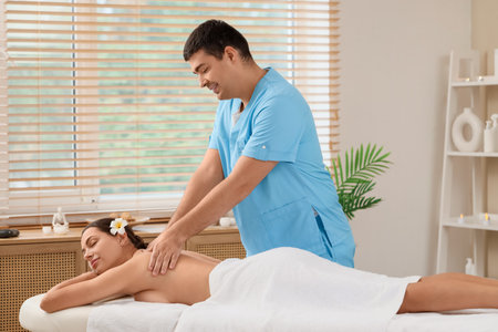 Male therapist massaging woman's back on couch in spa salonの写真素材