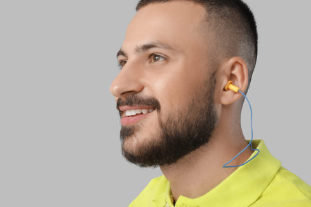 Young man with earplugs on gray background, closeup
