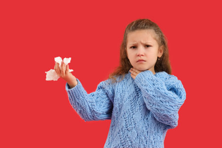 Sick little girl with sore throat and tissue on red backgroundの写真素材
