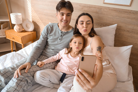 Little girl with her parents taking selfie in bedroomの写真素材