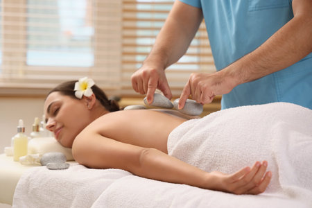 Young woman undergoing treatment with stones on couch in spa salonの写真素材