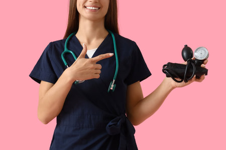 Young female doctor pointing at sphygmomanometer on pink background, closeupの写真素材
