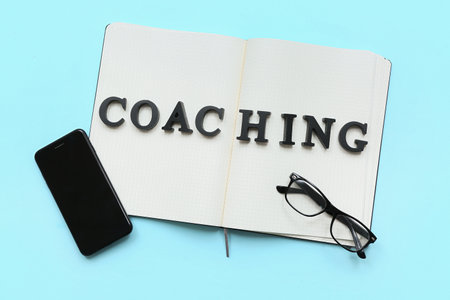Notebook with word COACHING, mobile phone and eyeglasses on blue backgroundの写真素材