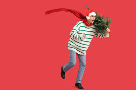 Young man with small Christmas tree running on red backgroundの写真素材