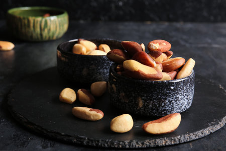 Bowls and board with tasty Brazil nuts on black background