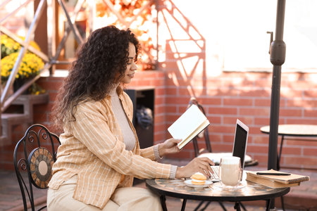 Young African-American author with laptop and notebook sitting at table in street cafeの写真素材