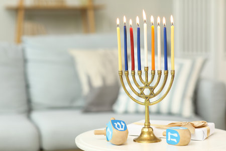 Menorah with burning candles, gift box and dreidels on table at home, closeup. Hanukkah celebrationの写真素材