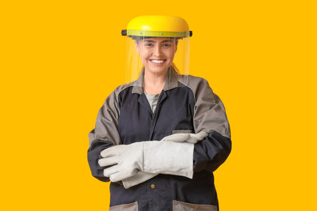 Young female construction worker with protective helmet and gloves on yellow background. Woman in male profession conceptの写真素材