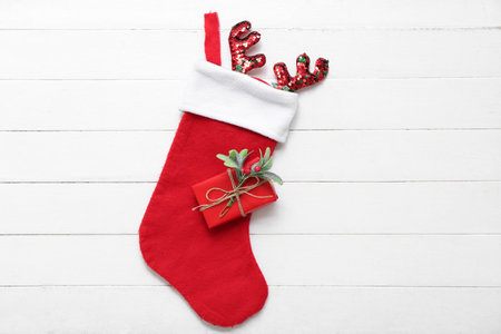 Christmas sock with reindeer horns, gift box and mistletoe twig on white wooden background. Top viewの写真素材