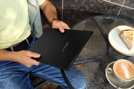 Young man with menu in street cafe, closeup