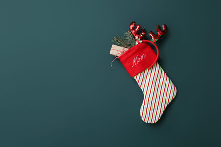 Christmas sock with reindeer horns, fir tree branch and gift hanging on green wall