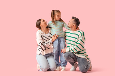 Happy family with their daughters in sweaters sitting on pink backgroundの写真素材