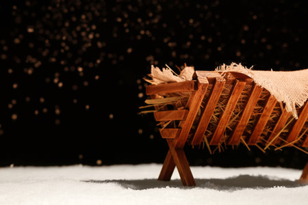 Manger with baby Jesus and hay on snow against dark backgroundの写真素材