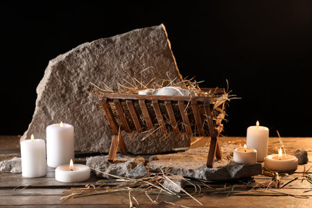 Manger with baby Jesus, rocks and burning candles on table against dark backgroundの写真素材