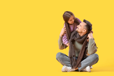 Happy father and his daughter in sweaters sitting on yellow backgroundの写真素材