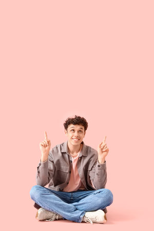 Handsome young man pointing at something on pink backgroundの写真素材