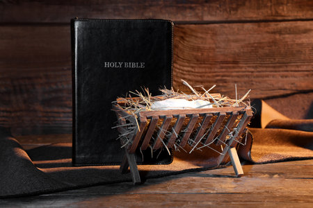 Manger with baby Jesus and Holy Bible on wooden table