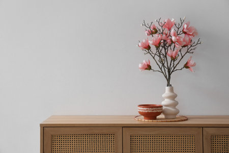 Vase with magnolia flowers on commode near gray wall