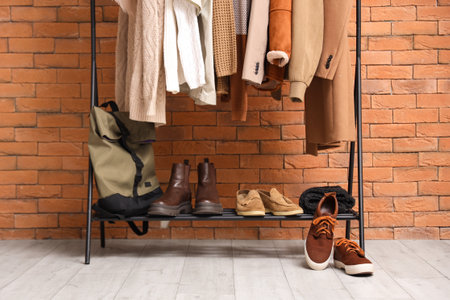 Rack with beige clothes and stand with shoes near brick wall. Closeupの写真素材