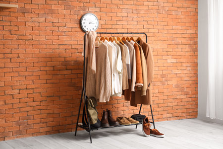 Rack with beige clothes and stand with shoes near brick wallの写真素材