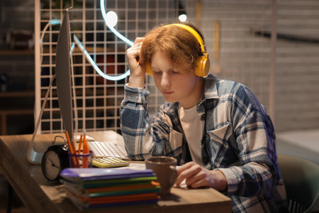 Male student with headphones studying in bedroom at nightの写真素材