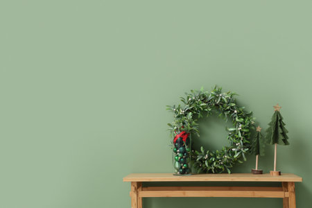 Bench with mistletoe wreath, box of Christmas balls and fir tree near green wall in roomの写真素材