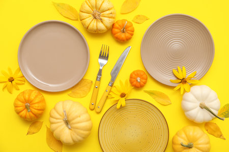 Beautiful table setting with fresh pumpkins, flowers and autumn leaves on yellow backgroundの写真素材