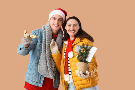 Cute young couple with tickets, wooden plane and small Christmas tree on beige background. Winter...