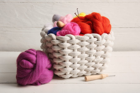 Basket with different wool for felting and needles on light wooden background