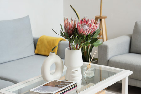 Protea flowers in vase with diffuser and magazines on glass coffee table in living room