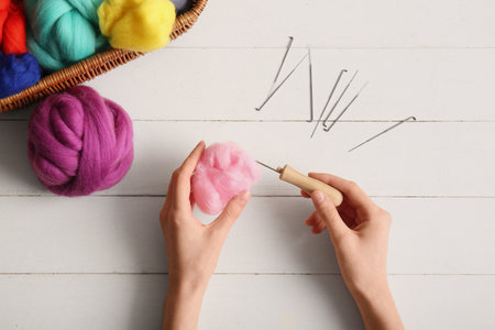 Female hands with wool for felting and needles on light wooden background, closeupの写真素材