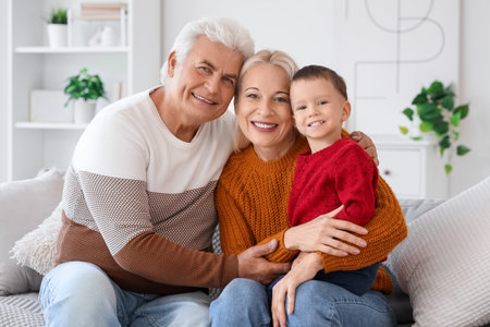 Cute little boy with happy grandparents sitting on sofa at home