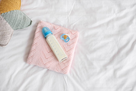 Bottle of baby milk formula, pacifier, plaid and cushion on light bed
