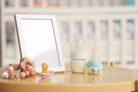Bottles of baby milk formula, pacifier, teether and blank picture frame on table in children's roomの写真素材