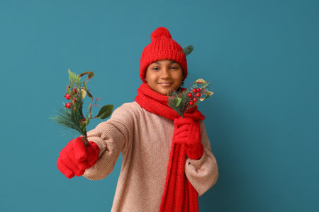 Cute African-American girl in stylish warm clothes with Christmas tree branches on blue backgroundの写真素材