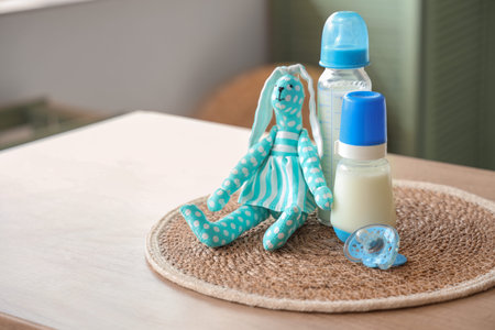 Bottles with baby milk formula, toy bunny and pacifier on wooden table at home