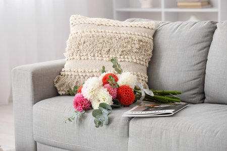 Bouquet of beautiful dahlia flowers and magazine on comfortable sofa in room