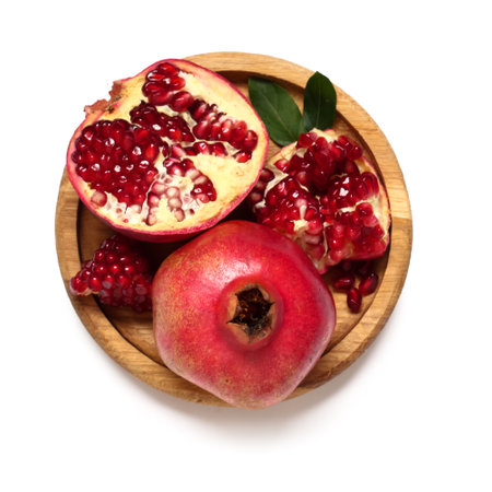 Wooden plate with fresh ripe pomegranates and leaves on white backgroundの写真素材