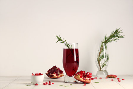 Glass of fresh pomegranate juice with rosemary and bowl of seeds on white tile tableの写真素材