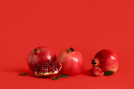 Fresh ripe pomegranates and leaves on red backgroundの写真素材
