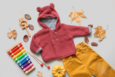 Composition with stylish baby clothes, toys and fallen leaves on gray backgroundの写真素材