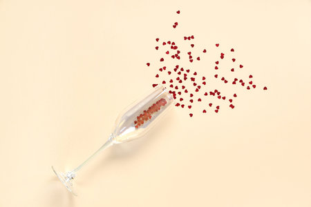 Champagne glass with confetti in shape of heart on beige background. Valentine's Day celebrationの写真素材
